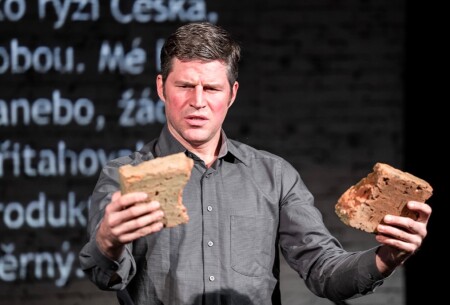 Der Schauspieler hält einen zerbrochenen Ziegelstein in der Hand und schaut ihn nachdenklich an.