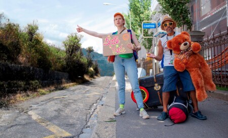 Eine junge Frau und ein Mann stehe am Strassenrand und machen Autostop