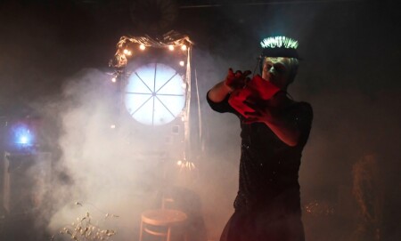 Die Dragqueen hat einen Lichterkranz auf dem Kopf. Das Foto ist sehr neblig und mit wenig Licht gemacht.